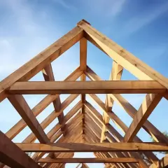 Drewniana konstrukcja dachu dwuspadowego, widok od dołu na tle błękitnego nieba.