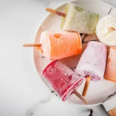 Variopinti ghiaccioli fatti in casa su un piatto bianco: rossi, arancioni, rosa, verdi e bianchi al cocco.