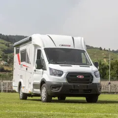 Porteur Ford camping-car blanc, prêt pour l'aventure sur un terrain verdoyant, avec des collines en arrière-plan.