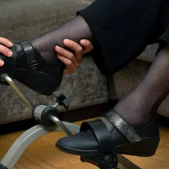 Osoba w białym stroju pomaga pacjentowi ćwiczyć na rowerku rehabilitacyjnym do wzmacniania mięśni rąk i nóg.