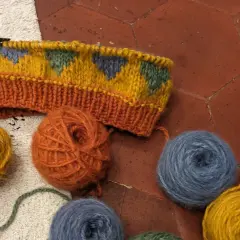 Un tricot jacquard aux motifs géométriques colorés, entouré de pelotes de laine.