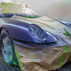 Lakiernik samochodowy przygotowuje auto do malowania. Samochód jest zakryty folią i taśmą, aby chronić elementy przed farbą.