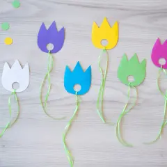 Bunte Papier-Tulpen mit grünen Bändern, perfekt für das Basteln mit Kindern. Bunte Tupfen liegen verstreut.