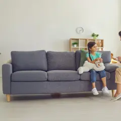 Psycholog dziecięcy rozmawia z dziewczynką siedzącą na kanapie z pluszowym misiem.