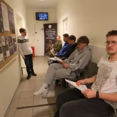 Młodzi ludzie czekają na komisję wojskową, przeglądając dokumenty. Na ścianie wiszą plakaty zachęcające do wstąpienia do wojska.