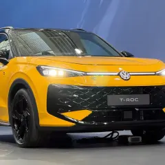 Żółty Volkswagen T-Roc z czarnym dachem i felgami. Zbliżenie na przód auta, widoczne światła LED i atrapa chłodnicy.