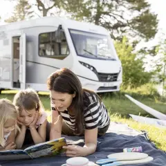 Rodzina czyta książkę przy kamperze samochód nad jeziorem. Dwie dziewczynki i mama cieszą się wspólnym czytaniem.