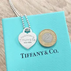 Srebrne serce z napisem "Please Return to Tiffany & Co. New York" na turkusowym pudełku Tiffany & Co. z monetą 2 złote.