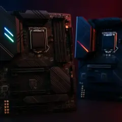 Deux cartes mères noires, l'une éclairée par des LED bleues et vertes, l'autre par des LED rouges, sur fond sombre.