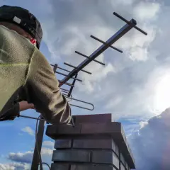 Osoba na dachu reguluje antenę naziemną. Chcesz wiedzieć, jak sprawdzić sygnał anteny naziemnej aplikacja? To zdjęcie może pomóc w ustawieniu.