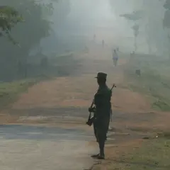 Ein Soldat mit Gewehr steht am Straßenrand, im Nebel sind schemenhaft Menschen und ein Fahrradfahrer zu sehen. Eine Szene, die an "die sieben Monde des Maali Almeida" erinnert.