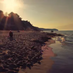 Zachód słońca nad morzem, ludzie spacerują brzegiem, w oddali majaczy wąwóz chłapowski.
