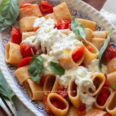 Piatto di pasta paccheri con pomodorini freschi e burrata cremosa, guarnito con basilico.
