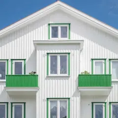 Vitt trähus med gröna detaljer runt fönster och balkonger. Ett perfekt hus att måla om för att fräscha upp.