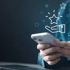 Dłoń trzymająca smartfon z ikoną gwiazdki i dłoni, symbolizującą ocenę.