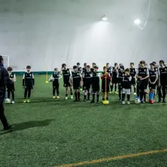 Trener prowadzi trening piłkarski metodą Coerver Coaching, instruując młodych zawodników na boisku.