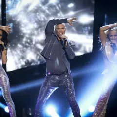 Yngves danskurser: Tre artister i glittriga scenkläder sjunger och dansar på en upplyst scen.