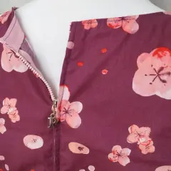 A plum-colored dress with a floral print features a centered zipper with a silver "P" charm.