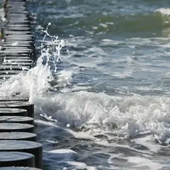 Fale rozbijają się o drewniane pale na plaży. Piękna, czerwcowa pogoda zachęca do spacerów brzegiem morza.