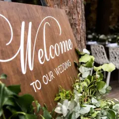Drewniana tablica "Welcome to our wedding" z zielonymi liśćmi. Zastanawiasz się, kogo zaprosić na wesele?