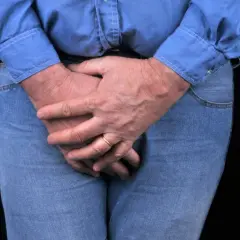 Homme aux mains croisées sur le devant, possiblement pour soulager une vessie hyperactive. L'électrostimulation peut aider.