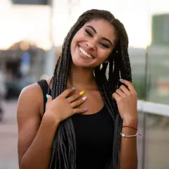 Joven sonriente con trenzas africanas, uñas de colores y un brazalete rojo.