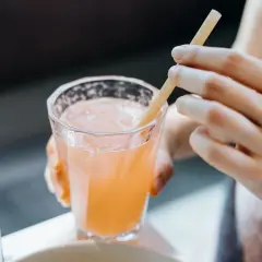 Glas mit rosafarbenem Getränk und Eis, eine Hand hält einen Strohhalm. Vielleicht ein gesunder Drink mit Sauerkrautsaft Inhaltsstoffe.