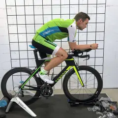Mężczyzna w stroju kolarskim na rowerze stacjonarnym podczas sesji bike fitting. Punkty pomiarowe na ciele i rowerze.