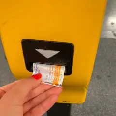 Dłoń z czerwoną hybrydą wkłada bilet do żółtego automatu w praskim metrze. Bilety na metro w Pradze są łatwe do kupienia.