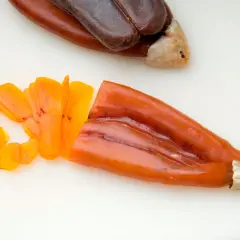Bottarga en español: huevas de pescado curadas, una entera oscura y otra naranja cortada en láminas finas.