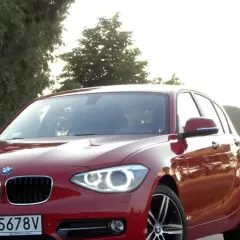 Czerwone BMW 118d na tle drzew i pól.