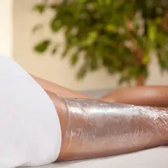 Zabieg body wrapping z użyciem kosmetyków. Nogi owinięte folią, przygotowane na odżywcze działanie.