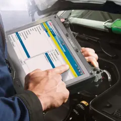 Mechanik sprawdza wtryski za pomocą tabletu diagnostycznego Bosch. Na ekranie widoczne są opcje wyboru systemu, w tym silnik i systemy sterowania.