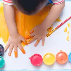 Manos pequeñas pintando con dedos y pincel. Un niño se divierte pintando con niños, rodeado de botes de pintura de colores.