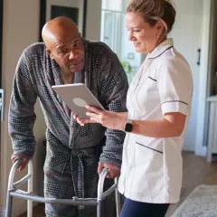 Pflegekraft zeigt Mann mit Gehhilfe auf Tablet, wie oft kann man eine Reha beantragen.