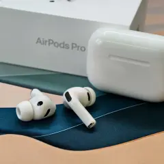 Białe słuchawki TWS AirPods Pro leżą obok pudełka i etui ładującego.