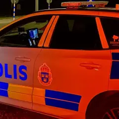 En polisbil med blåljus syns i mörkret. Texten "POLIS" är tydlig på sidan.
