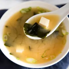 A spoonful of savory miso sauce soup, with tofu cubes and seaweed, ready to be enjoyed.