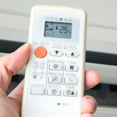 Mano sujetando control remoto de aire acondicionado. El símbolo del triángulo indica la función de enfriamiento.
