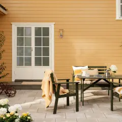 Ett gult hus med svart tak. En uteplats med gröna möbler, blommor och en orange pläd.