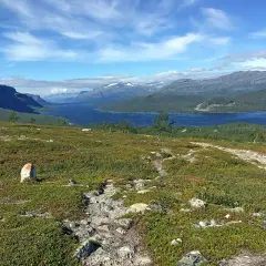 Vacker vy över en sjö och berg, med en stenröse markerad med rött. En vandringsled leder mot horisonten, kanske på väg mellan Kvikkjokk och Saltoluokta.