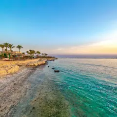 Piękna pogoda w Marsa Alam: piaszczysta plaża z palmami, leżakami i parasolami, turkusowe morze i długie molo na horyzoncie.