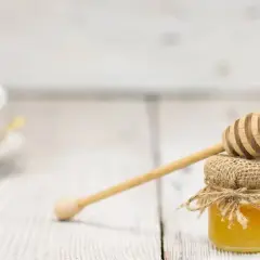Mały słoiczek miodu z drewnianą chochlą, idealny do słodzenia herbaty. Łyżka miodu kcal to tylko dodatek do pysznego smaku.