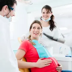 Uśmiechnięta ciężarna pacjentka u dentysty. Dba o zdrowie jamy ustnej, by uniknąć zapalenia dziąseł w ciąży.