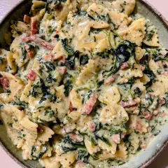 Pyszny makaron farfalle w kremowym sosie ze szpinakiem i kawałkami boczku. Idealny makaron ze szpinakiem i serem na szybki obiad.