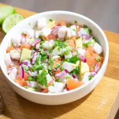 Pyszne ceviche z kawałkami ryby, awokado, grejpfruta, czerwonej cebuli i kolendry, podane w białej misce.