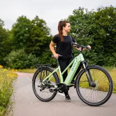 Młoda kobieta z rowerem elektrycznym na ścieżce wśród łąki. Od ilu lat można jeździć na rowerze elektrycznym?