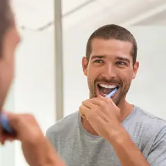 Uomo sorridente si lava i denti davanti allo specchio, un gesto quotidiano per la prevenzione odontoiatrica.