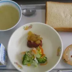 A typical Japanese school lunch tray with soup, bread, vegetables, meat, pudding, and milk.