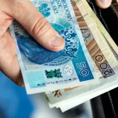 Dłoń trzyma polskie banknoty, w tym 50 i 200 zł, przygotowując się do wypłaty zasiłku pogrzebowego.
